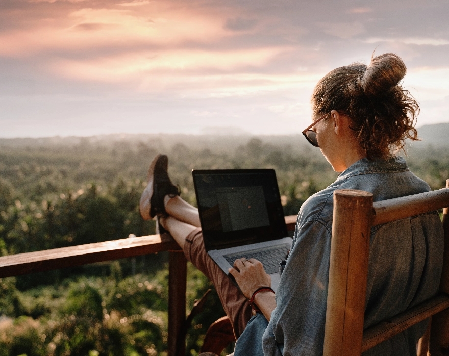 a woman working remotely on a balcony overlooking a forest